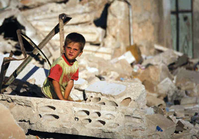 Một em bé Syria đứng cạnh căn nhà đổ nát do giao tranh ở thị trấn Taftanaz.